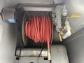 A coiled red air hose mounted on a reel with a metal connector and two yellow valves attached to pipes in a machinery compartment