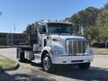 A 2020 Peterbilt 330 truck with a flatbed and chrome details parked on a street with an upright front grille and multiple amber lights on the roof