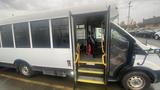 A 2021 Ford Transit shuttle bus with an open door revealing interior seating and yellow handrails