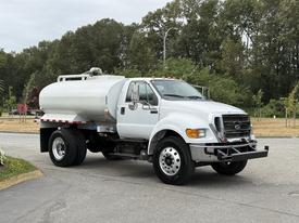 White 2013 Ford F-750 truck with a large cylindrical tank in the bed and multiple wheels displayed in the foreground