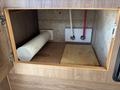 An empty cabinet featuring a cylindrical white container and a wooden board resting on the floor with two connections visible on the wall