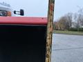 A close-up of a red snow plow blade with a measuring tape indicating its height