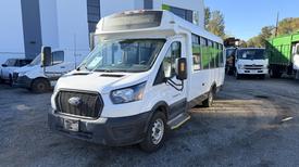A white 2021 Ford Transit shuttle bus with a large front grille and multiple windows on the side