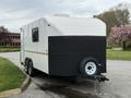 A 2025 Shuttle Office is a compact trailer with a white body and black lower section featuring two wheels and a hitch in front