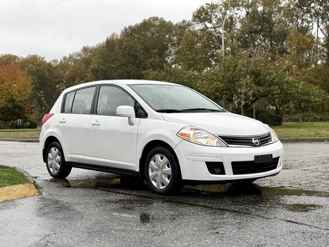A 2012 Nissan Versa in white with a hatchback design parked on a wet surface