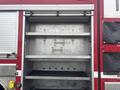 A metallic storage compartment with three shelves inside a red fire truck, featuring two metal hooks attached to the back wall