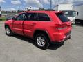 A red 2015 Jeep Grand Cherokee parked with its door slightly open and wheels equipped for off-road driving