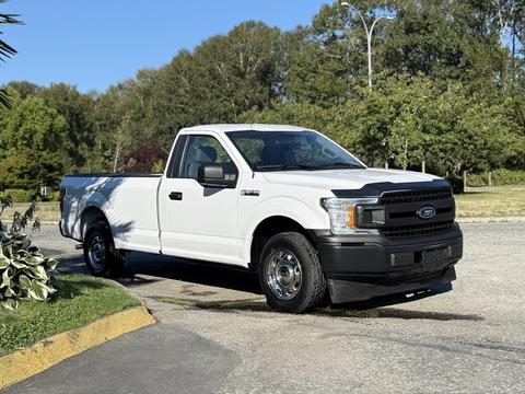 A white 2018 Ford F-150 pickup truck parked in a lot with a single cab and bed, featuring a black grille and wheels