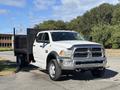A white 2014 RAM 5500 truck with a flatbed design and a chrome grille parked on a road