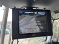 A monitor displaying a rearview camera feed showing a curved road and surrounding area in a vehicle cabin