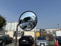 A round side mirror reflecting the cab of a white 2020 Peterbilt 330 truck with part of a parked car visible in the foreground