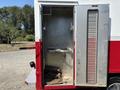An open metal cabinet on a 2007 GMC C4500 TopKick featuring a shelf and hooks inside with a beige mat on the floor