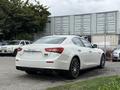 A white 2016 Maserati Ghibli with sleek lines and distinctive design features parked with its rear view facing the camera