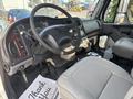 Interior view of a 2010 Freightliner M2 106 with a black steering wheel gray leather seat and various control dials and levers visible on the dashboard and console