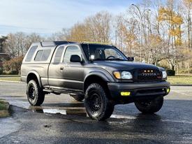 A black 2004 Toyota Tacoma with larger tires and a raised suspension features a cap on the bed and a light bar on the roof