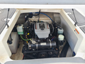 An exposed engine of a 2013 Larson 238 boat featuring a gray engine cover with a logo multiple hoses and fluid containers visible around the engine components