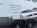 A 2013 Outdoor Wind River trailer featuring a white exterior with gray accents and black wheels along with a service panel and various labels on the side