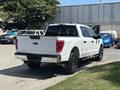 A white 2021 Ford F-150 with black rims and a crew cab is parked, showing its rear and side profile