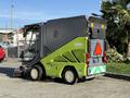 A 2015 Tennant 636 Green Machine street sweeper with a green and gray exterior featuring a triangular warning sign on the back and equipped with a front brush for cleaning