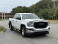 A white 2016 GMC Sierra 1500 pickup truck with a chrome grille and side steps parked on a gravel surface