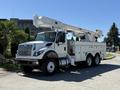 A white 2013 International 7400 bucket truck with an extended boom and utility storage compartments on the side parked in a lot