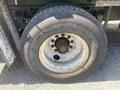 Close-up of a tire mounted on a white rim with visible rust and wear the tire shows the brand name Goodyear and is attached to a Freightliner FL70 truck