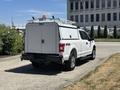 A white 2019 Ford F-150 with a utility cap on the bed and a roof rack is parked on a concrete surface