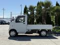 A white 2009 Suzuki Carry truck viewed from the side with a flatbed design and small wheels
