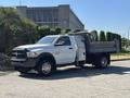 A white 2016 RAM 5500 pickup truck with a flatbed and storage compartments on the side parked on a concrete surface