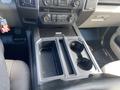 Interior view of a 2015 Ford F-150 center console featuring two cup holders and various controls for audio and climate settings
