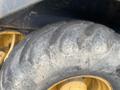 Close-up of a large, worn tire from a 2012 John Deere 310SJ construction vehicle featuring deep treads and a yellow rim