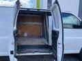 A 2023 GMC Savana van with its double rear doors open showcasing an empty cargo area with a wooden wall and a steel loading strip