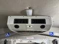 An overhead air conditioning unit with two vents mounted inside a vehicle, featuring a logo and indicators for emergency exit and accessibility