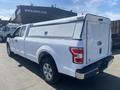 A white 2019 Ford F-150 pickup truck with a hard-shell bed cover shown from the rear side angle