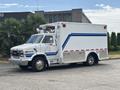 A white 1994 GMC Vandura 3500 ambulance with blue stripes and a light bar on top parked on a street