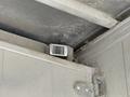 A small rectangular sensor mounted on the interior corner of a truck trailer with a metallic surface and visible dust accumulation