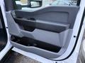 The interior door panel of a 2023 Ford F-250 featuring a speaker a handle and storage compartments in gray and black plastic
