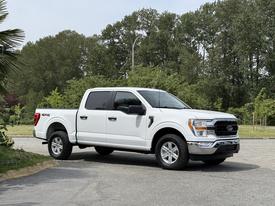 A white 2021 Ford F-150 with a crew cab parked in a semi-turned position showcasing its side and front features