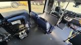 Interior of a 2021 Ford Transit showing three seats including two blue seats facing forward and one seat folded against the wall with a console and dashboard visible