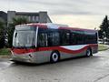 A red and white 2016 Grande West Vicinity bus with a modern design and large windows parked on a street