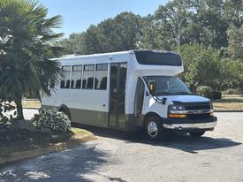 A white 2020 Chevrolet Express bus is parked with its door open showing a spacious interior designed for passenger transport