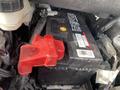 A black car battery with a red protective cover and labels, positioned within the engine compartment of a 2017 Ford Edge