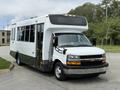 A 2020 Chevrolet Express shuttle bus with a white exterior and large windows parked at an angle showing its front and side features