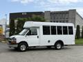 A 2013 Chevrolet Express white shuttle bus with large windows and a raised roof parked on a concrete surface