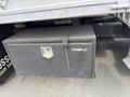 A black metal toolbox mounted under a truck with a secure latch and rust marks visible on its surface