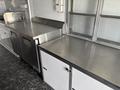 A metal countertop with an integrated sink and a refrigerator unit on the left side next to a flat work surface on the right side inside a vehicle interior