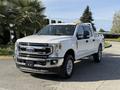 A 2021 Ford F-250 SD pickup truck in white with a chrome grille and wheels parked in a lot