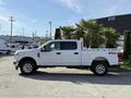 A white 2021 Ford F-250 Super Duty truck with chrome rims and a flatbed design parked beside palm trees