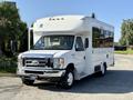 A white 2016 Ford Econoline bus with a wheelchair lift and large side windows parked on a paved surface