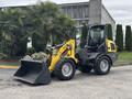 A 2014 Wacker Neuson WL34 compact wheel loader with a bucket attachment in a landscaped setting